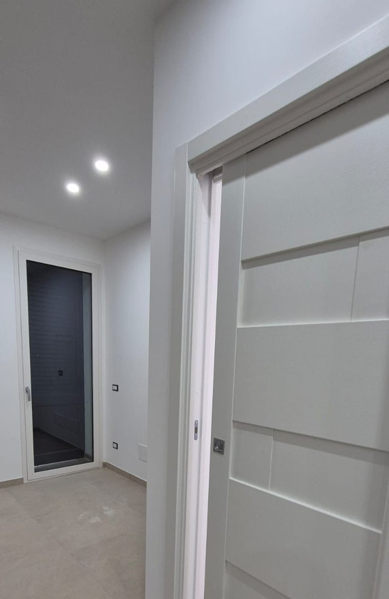 Un vano con porta scorrevole a filo muro, in un corridoio illuminato